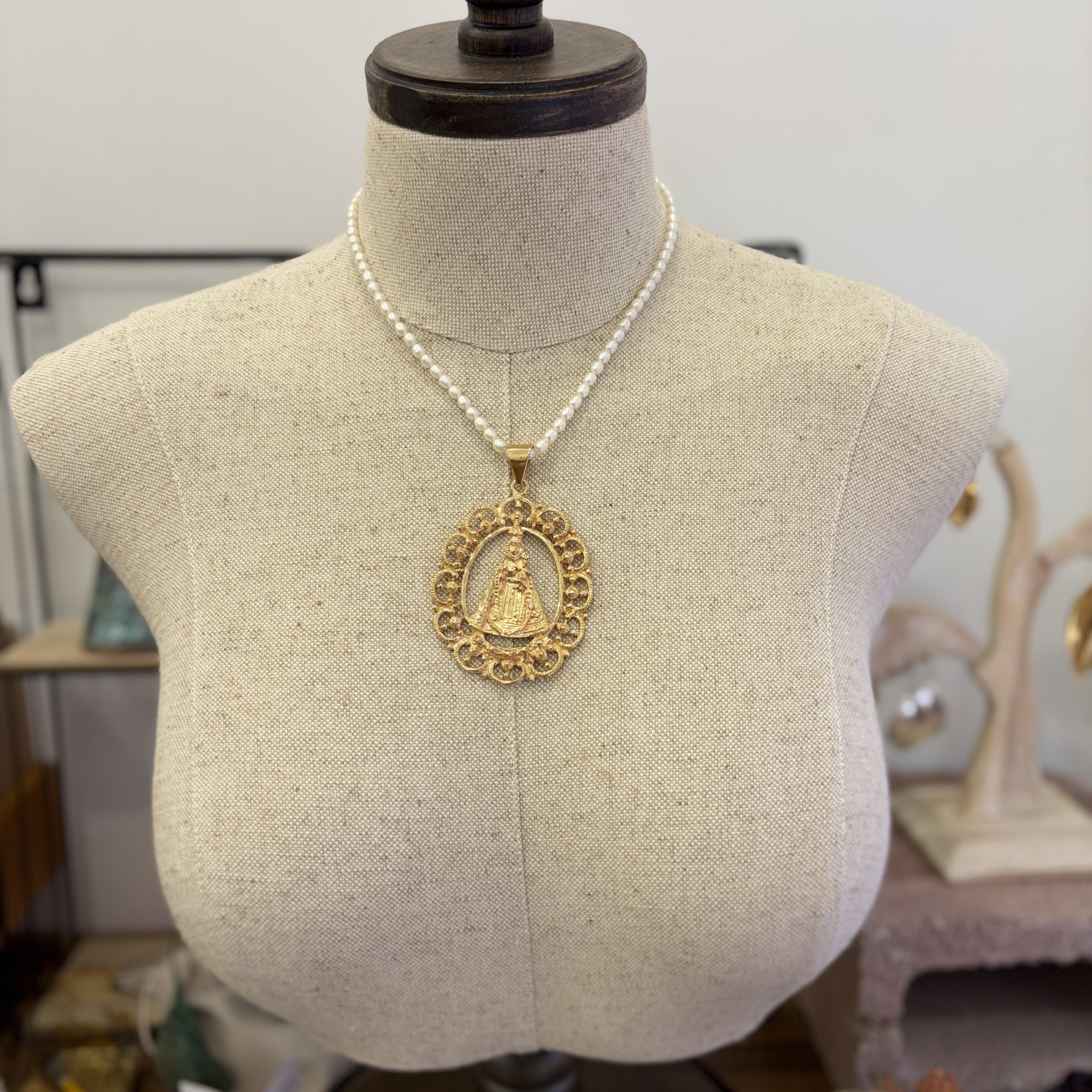 Medalla de plata con recubrimiento de oro de 24K junto a un collar de perlas naturales